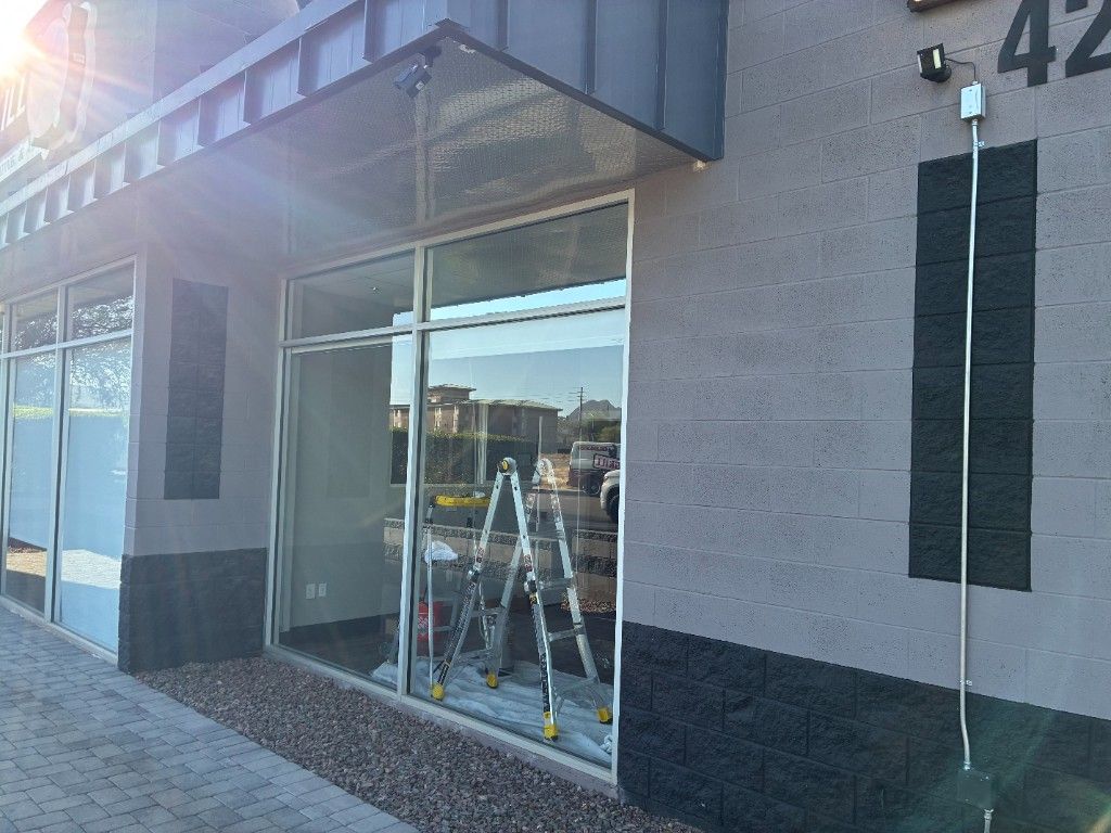 Exterior view of an Arizona commercial storefront under a metal awning, with reflective film on the windows and installation prep visible through the glass.