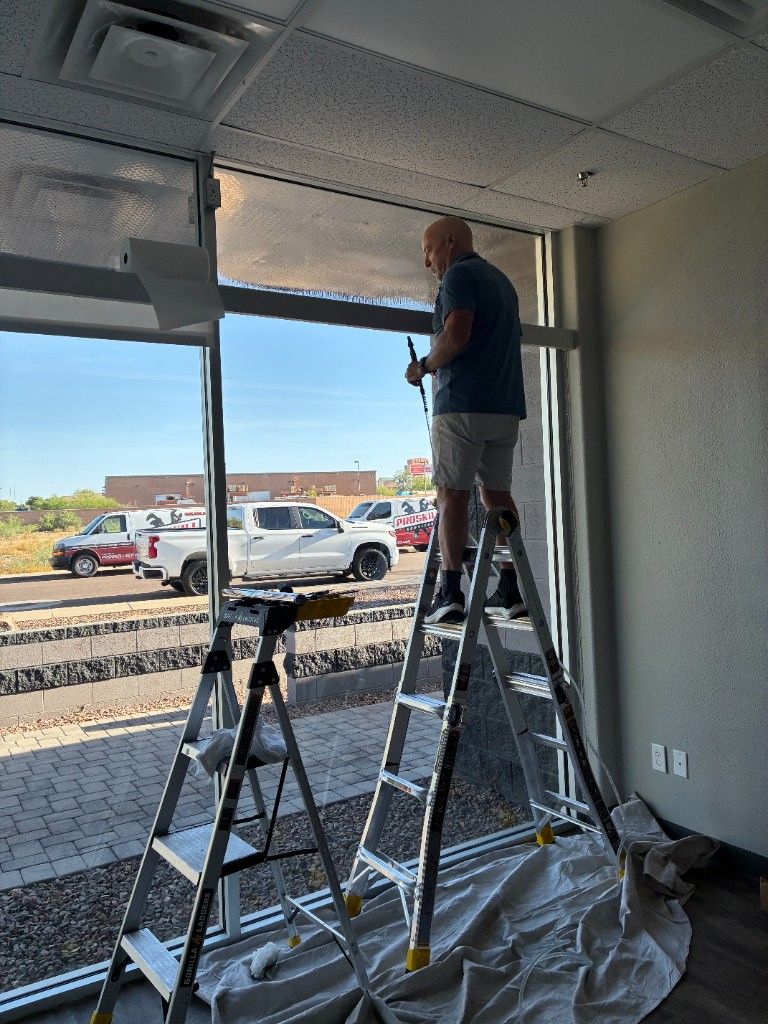 Interior commercial window film installation in Arizona—installer on a ladder working the upper glass while ProSkill-branded vans are visible through the window in the parking lot.