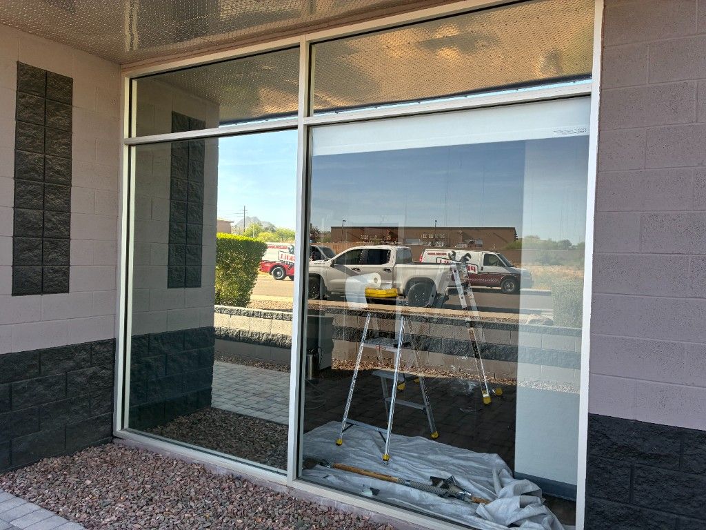Arizona commercial storefront during window film installation—ladder and floor protection inside, with ProSkill service vehicles reflected in the glass.